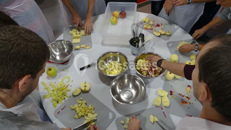 Des personnes épluchent et découpent des pommes autour d'une table avec des bols et des ustensiles de cuisine.
