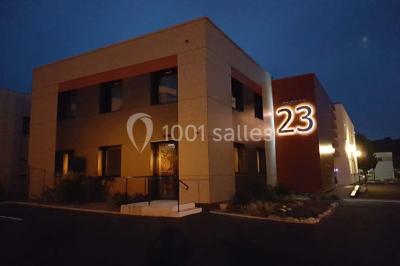 Un petit pont en bois traverse un bassin entouré de végétation, avec une route et des bâtiments en arrière-plan.