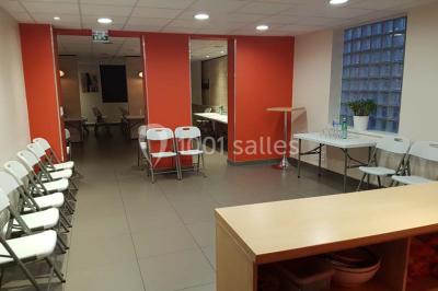 Un petit pont en bois traverse un bassin entouré de végétation, avec une route et des bâtiments en arrière-plan.