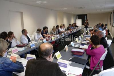 Bâtiment moderne à deux étages avec façade grise et rouge, entouré d'un parking et clôturé par une grille noire.