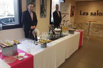 Bâtiment moderne à deux étages avec façade grise et rouge, entouré d'un parking et clôturé par une grille noire.