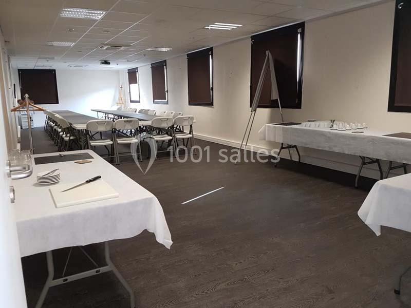 Salle de réunion avec tables et chaises alignées, éclairage artificiel et rideaux fermés.