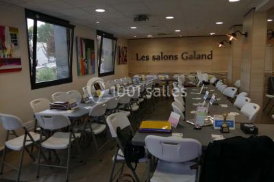 Bâtiment moderne à deux étages avec façade grise et rouge, entouré d'un parking et clôturé par une grille noire.