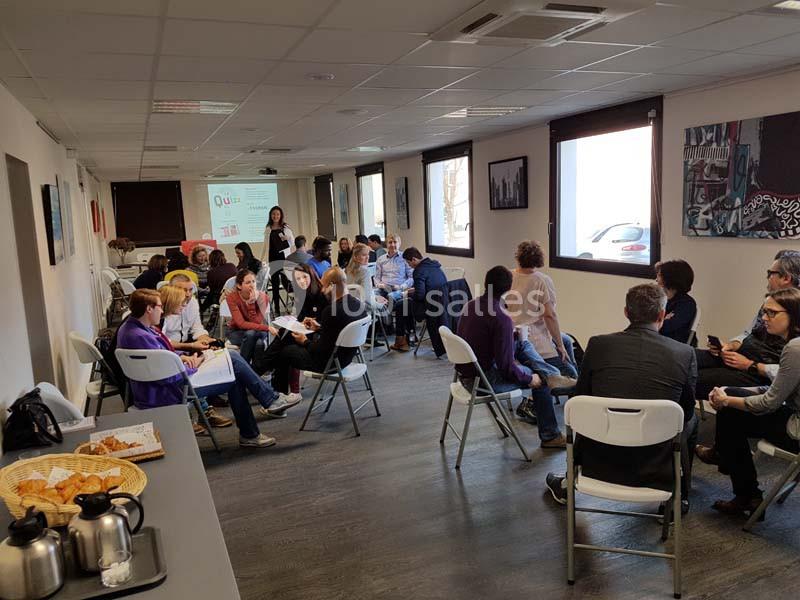 Des personnes assises en petits groupes discutent dans une salle lumineuse équipée de chaises et d'un projecteur.
