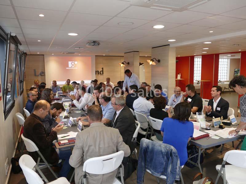 Groupe de personnes assises autour de tables lors d'une réunion dans une salle lumineuse.