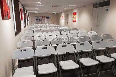 Bâtiment moderne à deux étages avec façade grise et rouge, entouré d'un parking et clôturé par une grille noire.