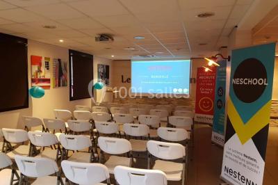 Bâtiment moderne à deux étages avec façade grise et rouge, entouré d'un parking et clôturé par une grille noire.