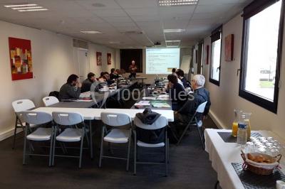 Bâtiment moderne à deux étages avec façade grise et rouge, entouré d'un parking et clôturé par une grille noire.