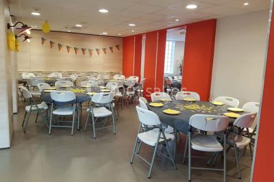 Bâtiment moderne à deux étages avec façade grise et rouge, entouré d'un parking et clôturé par une grille noire.