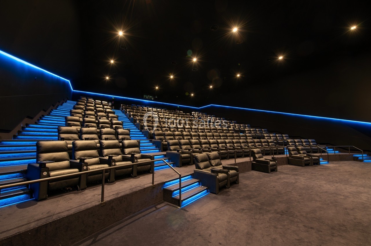 Salle de cinéma moderne avec sièges en cuir noir, éclairage bleu le long des escaliers et plafond sombre.