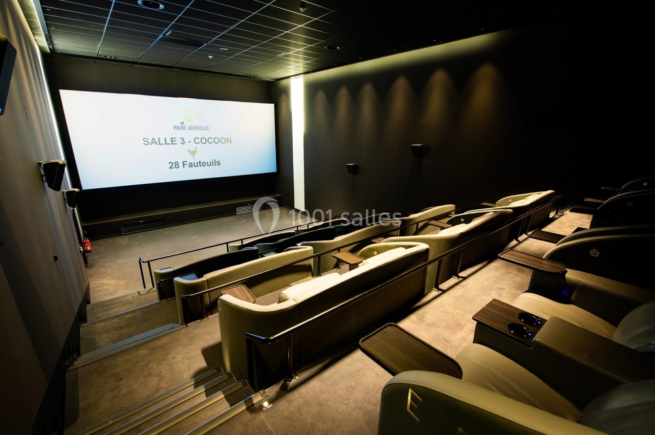 Salle de cinéma moderne avec fauteuils inclinables en cuir, écran allumé et éclairage tamisé.
