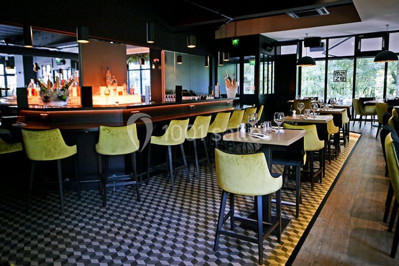 Salle de restaurant moderne avec bar éclairé, chaises jaunes et tables dressées sur un sol à motifs géométriques.