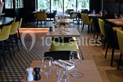 Salle de restaurant moderne avec bar central, tabourets jaunes, tables dressées et éclairage tamisé.