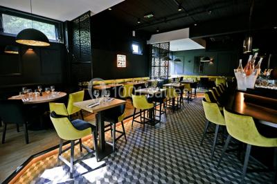 Salle de restaurant moderne avec bar central, tabourets jaunes, tables dressées et éclairage tamisé.