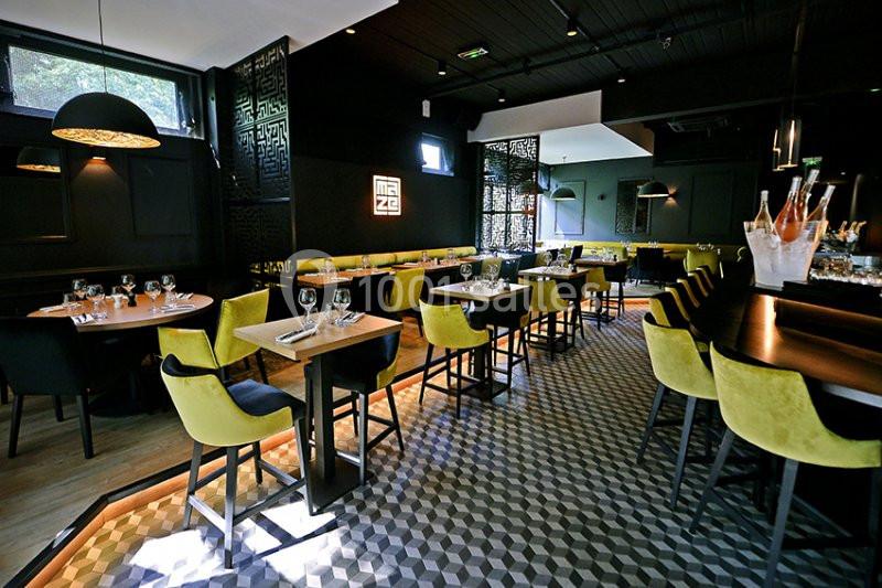 Salle de restaurant moderne avec tables dressées, chaises jaunes et noires, éclairage tamisé et sol à motifs géométriques.