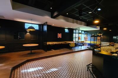 Salle de restaurant moderne avec bar central, tabourets jaunes, tables dressées et éclairage tamisé.