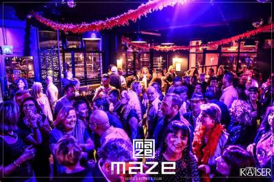 Salle de restaurant moderne avec bar central, tabourets jaunes, tables dressées et éclairage tamisé.