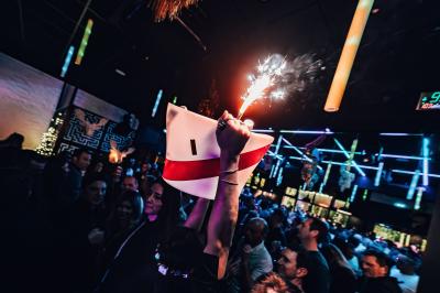 Salle de restaurant moderne avec bar central, tabourets jaunes, tables dressées et éclairage tamisé.