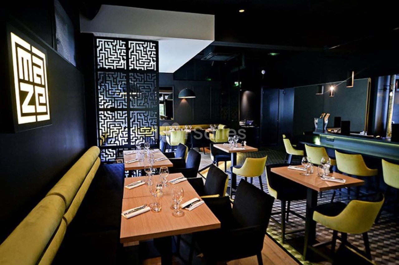 Salle de restaurant moderne avec tables en bois, chaises jaunes, banquettes vertes et éclairage tamisé.