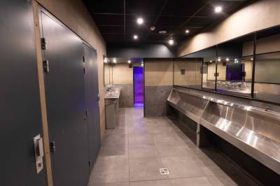 Salle de toilettes modernes avec lavabos en acier inoxydable, miroirs, cabines fermées et éclairage au plafond.