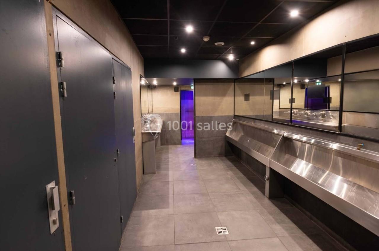 Toilettes publiques modernes avec urinoirs en acier inoxydable, lavabos et éclairage tamisé.