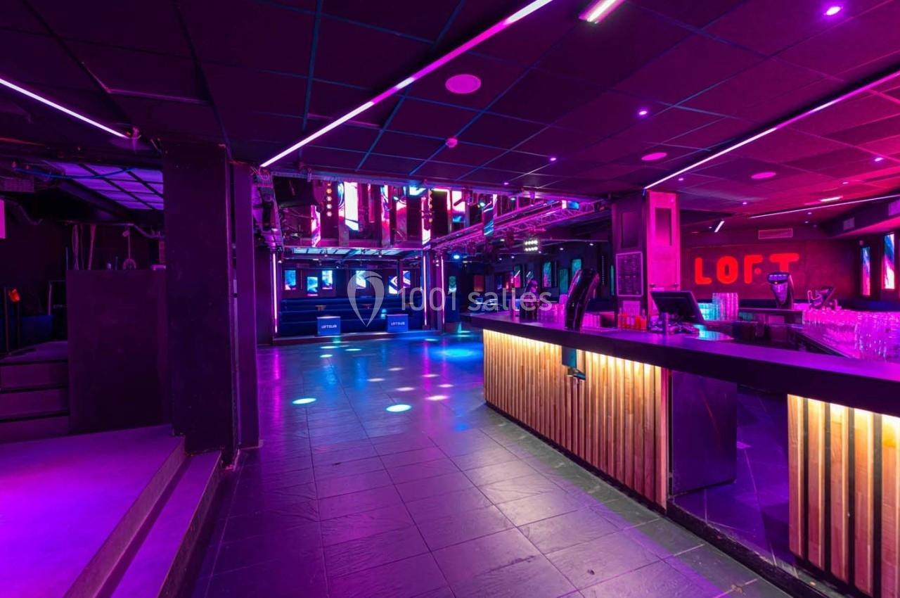 Intérieur d'une discothèque avec piste de danse éclairée par des lumières colorées et un bar en bois à droite.