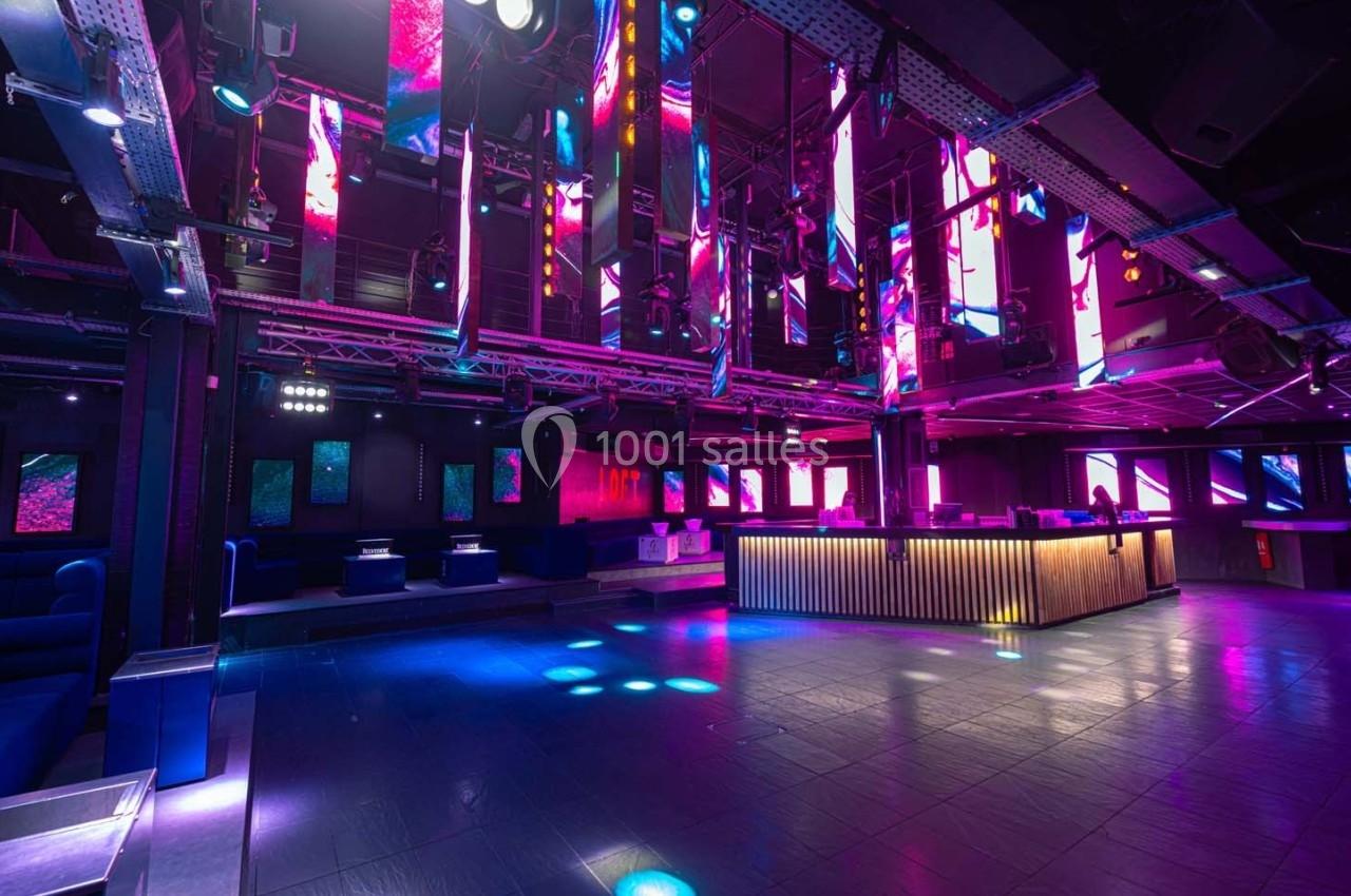 Salle de discothèque moderne avec éclairage coloré, piste de danse vide et comptoir lumineux en bois.