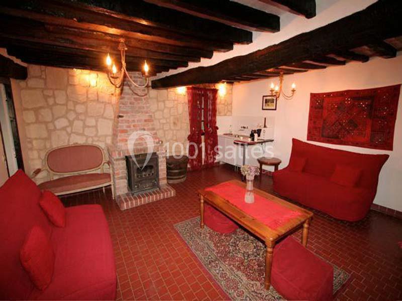 Salon rustique avec murs en pierre, poutres apparentes, canapé rouge, cheminée en brique et table basse en bois.