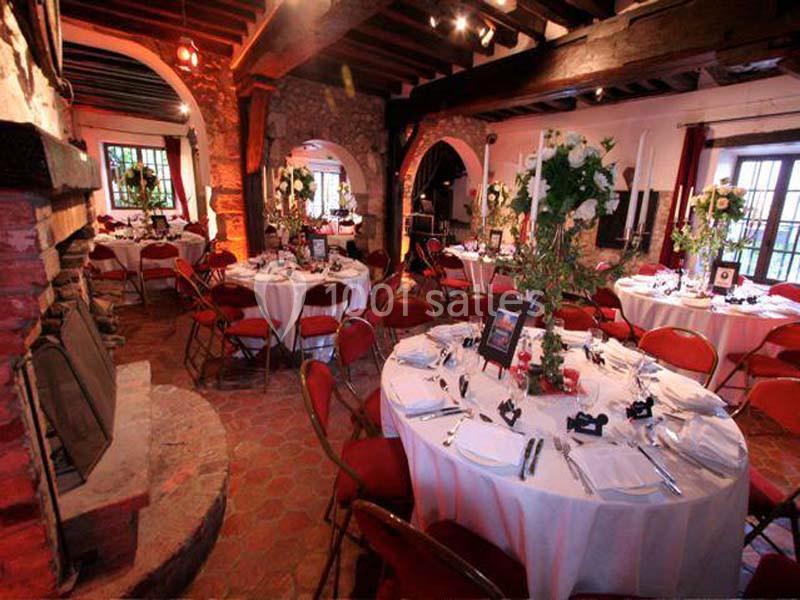 Salle de réception rustique avec tables rondes dressées pour un événement, entourées de chaises rouges.