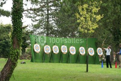 Cibles de tir à l'arc alignées sur un terrain herbeux, entourées d'arbres, avec deux personnes à proximité.