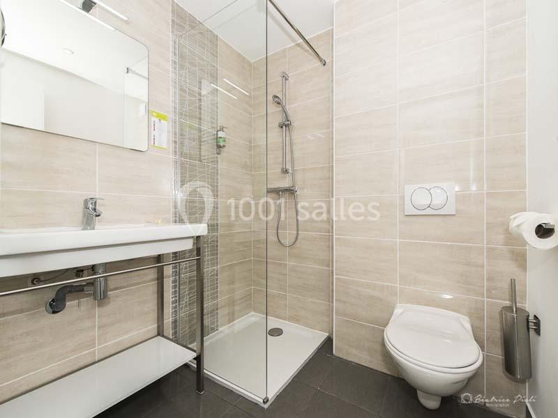 Salle de bain moderne avec douche à l'italienne, lavabo suspendu, toilettes murales et carrelage beige.