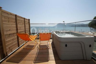Chambre lumineuse avec lit double, décor beige et fenêtre ouverte offrant une vue sur la mer et les collines.