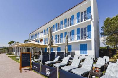 Chambre lumineuse avec lit double, décor beige et fenêtre ouverte offrant une vue sur la mer et les collines.