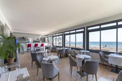 Chambre lumineuse avec lit double, décor beige et fenêtre ouverte offrant une vue sur la mer et les collines.