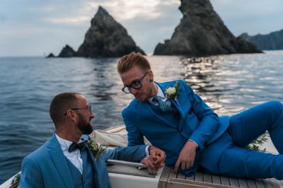 Chambre lumineuse avec lit double, décor beige et fenêtre ouverte offrant une vue sur la mer et les collines.