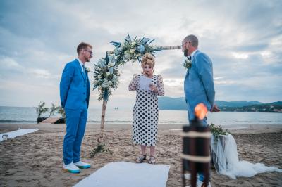 Chambre lumineuse avec lit double, décor beige et fenêtre ouverte offrant une vue sur la mer et les collines.