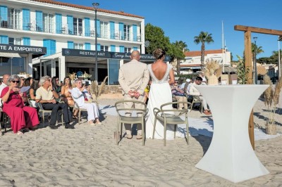 Chambre lumineuse avec lit double, décor beige et fenêtre ouverte offrant une vue sur la mer et les collines.