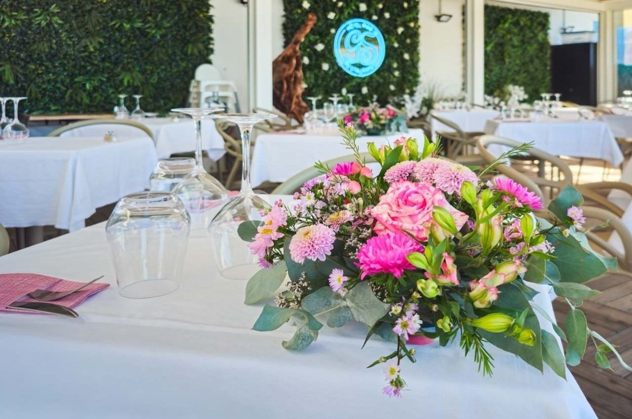 Bouquet de fleurs roses et blanches sur une table dressée dans un restaurant avec mur végétal en arrière-plan.