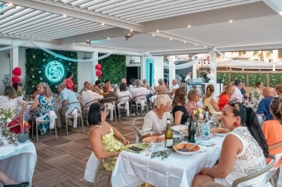 Chambre lumineuse avec lit double, décor beige et fenêtre ouverte offrant une vue sur la mer et les collines.