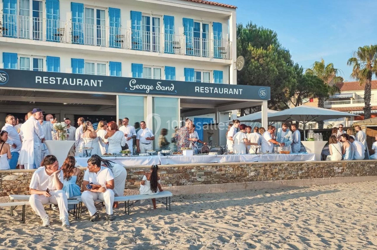 Groupe de personnes en tenue blanche rassemblées devant un restaurant en bord de plage par une journée ensoleillée.