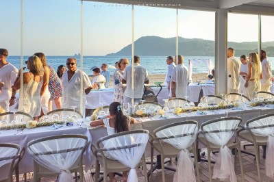 Chambre lumineuse avec lit double, décor beige et fenêtre ouverte offrant une vue sur la mer et les collines.