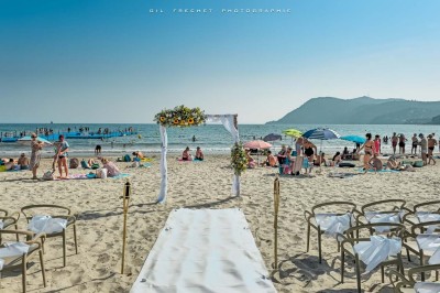 Chambre lumineuse avec lit double, décor beige et fenêtre ouverte offrant une vue sur la mer et les collines.