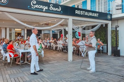 Chambre lumineuse avec lit double, décor beige et fenêtre ouverte offrant une vue sur la mer et les collines.