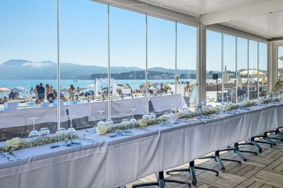 Chambre lumineuse avec lit double, décor beige et fenêtre ouverte offrant une vue sur la mer et les collines.