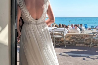 Chambre lumineuse avec lit double, décor beige et fenêtre ouverte offrant une vue sur la mer et les collines.