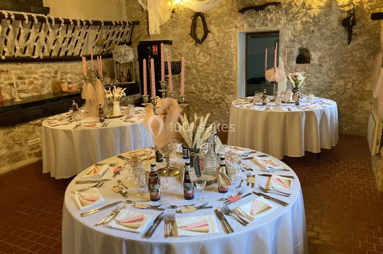 Salle en pierre décorée pour un événement, avec des tables rondes dressées, nappes blanches et décorations élégantes.