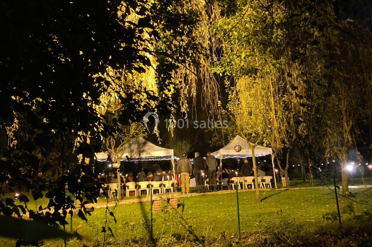 Des tentes éclairées installées dans un parc la nuit, entourées d'arbres et de végétation.
