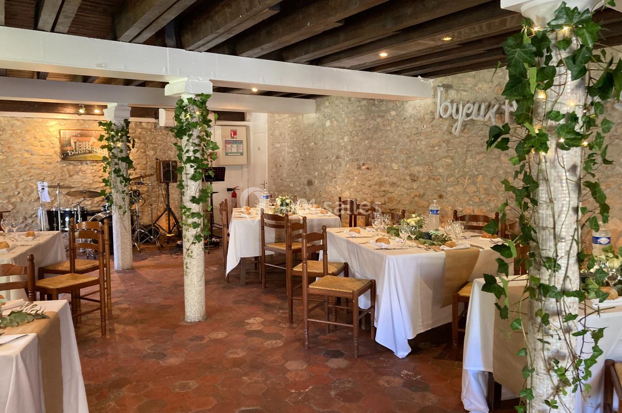 Salle de réception rustique avec tables dressées, chaises en bois, murs en pierre et décorations de lierre.