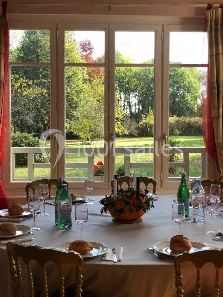Table dressée avec vaisselle, pain et bouteilles d'eau, devant une baie vitrée donnant sur un jardin verdoyant.