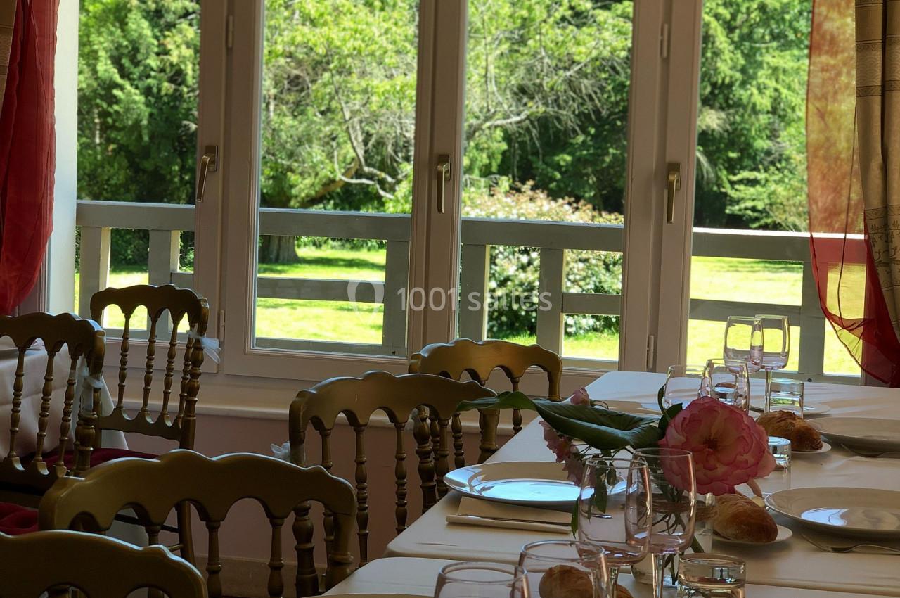 Table dressée avec vaisselle, verres et pain, devant une fenêtre ouverte sur un jardin verdoyant.